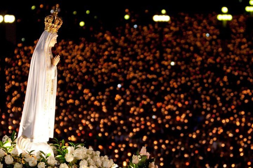 A statue with a crown, surrounded by white flowers, with a blurred background of lights. 2