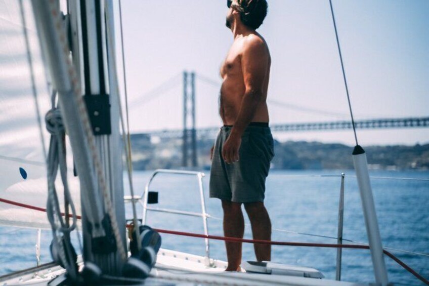 A person standing on a sailboat with a bridge in the background. 1