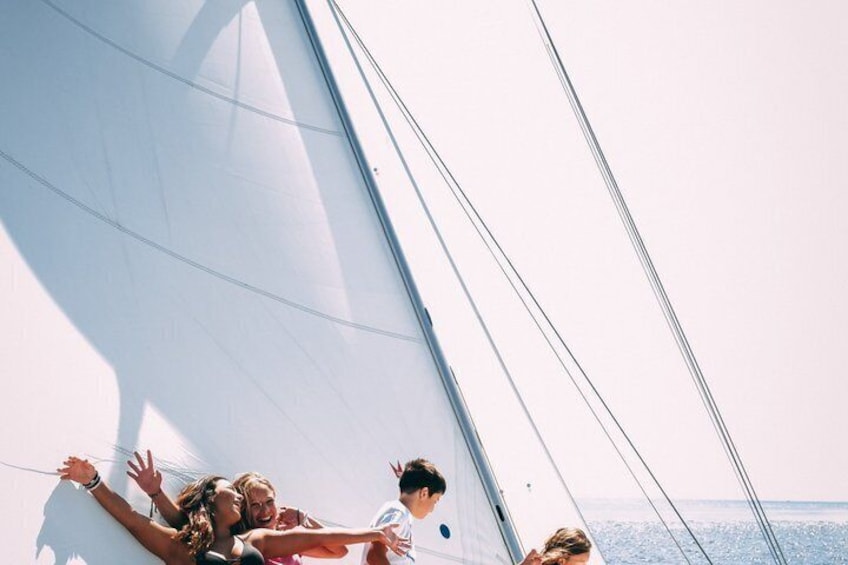 A sailboat with people on deck, a clear sky, and calm sea. 5
