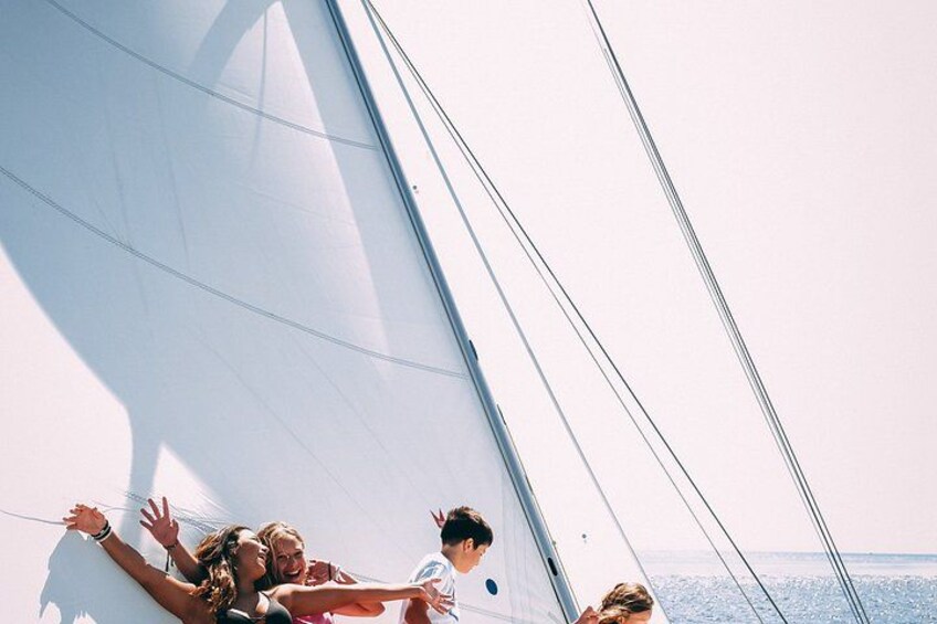 A sailboat with people on deck, a clear sky, and the ocean in the background. 5