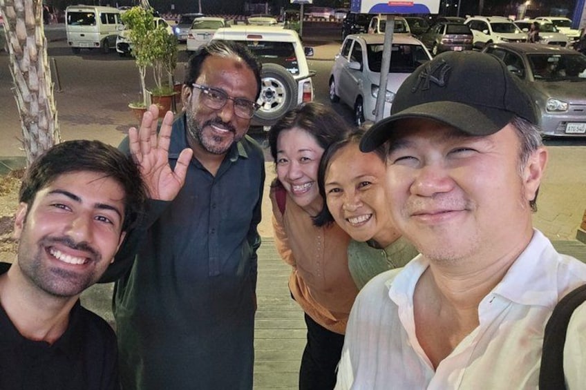 A group of people posing for a photo in an outdoor setting with parked cars and a tree in the background. 5
