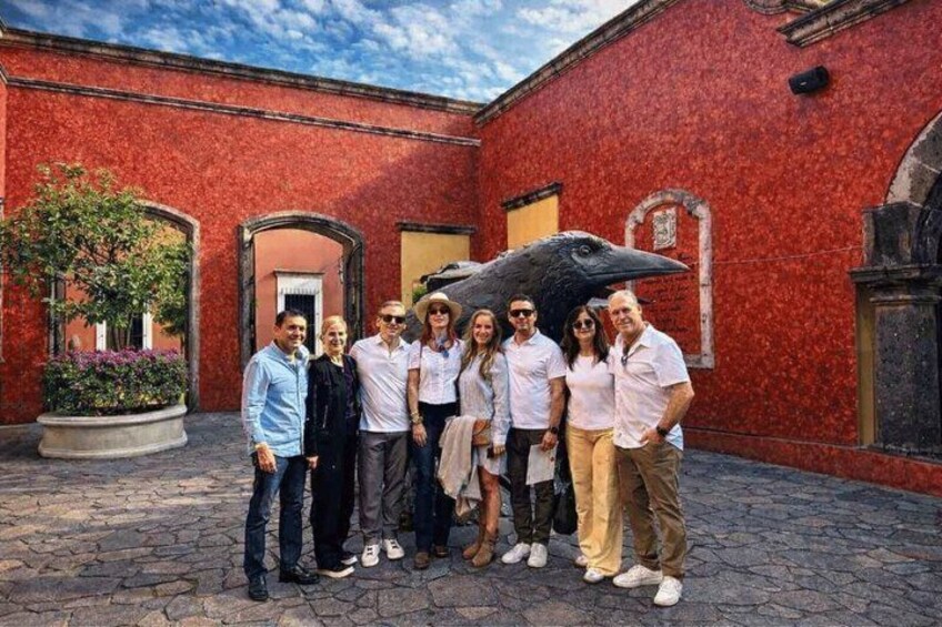 A group of people standing in a courtyard with red brick walls and a large bird sculpture. 3