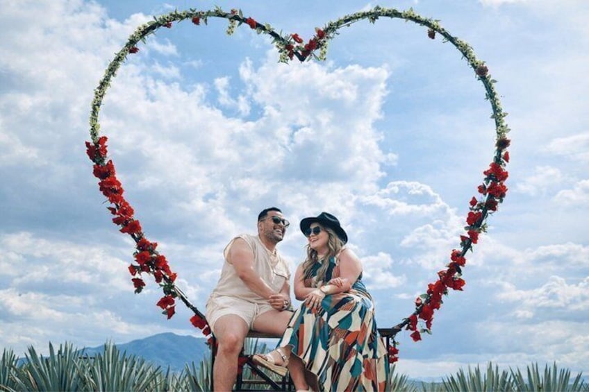 A couple seated under a heart-shaped floral arch with a mountainous backdrop. 1