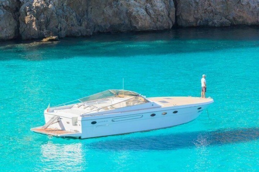 A white yacht anchored in clear turquoise water with rocky cliffs in the background. 1