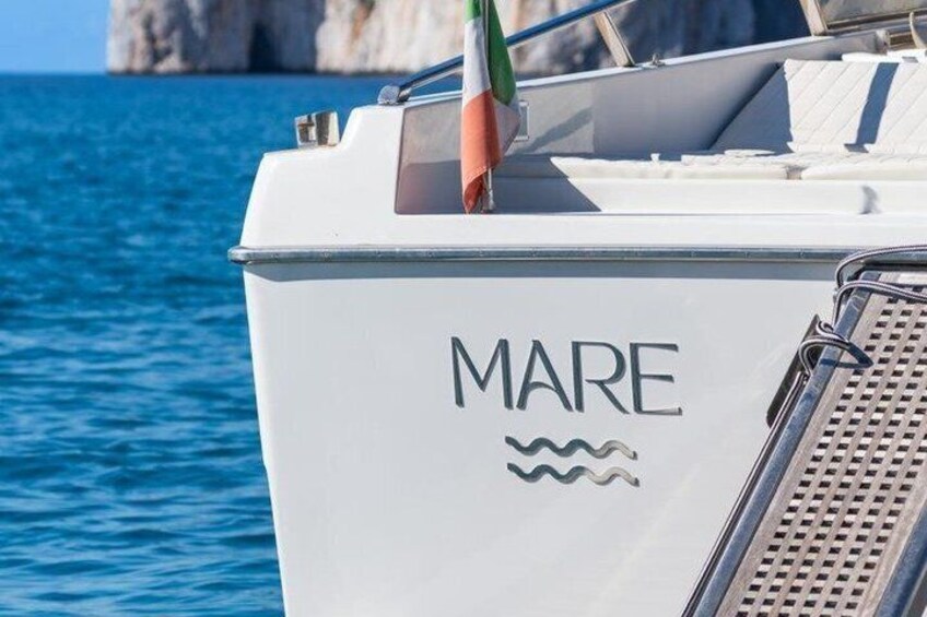 A boat with 'MARE' written on its side, a flag, and a rocky coastline in the background. 3