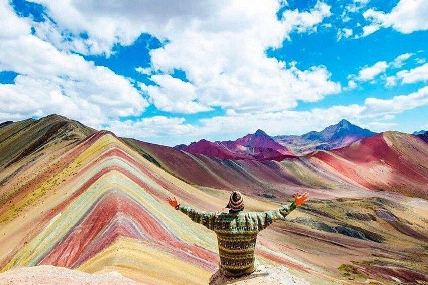 A person standing with arms outstretched, facing a colorful mountain landscape. 2