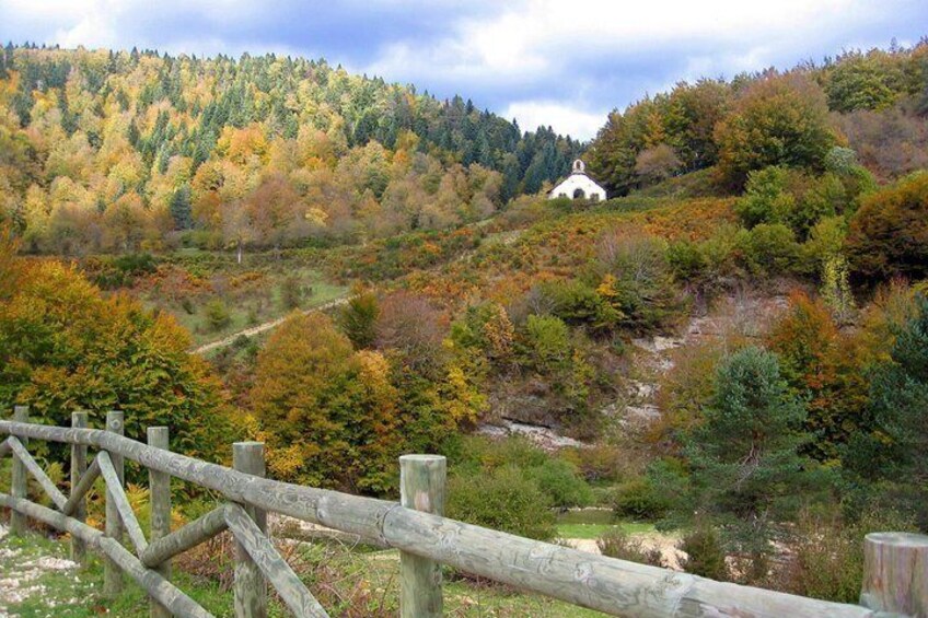 A wooden fence, a white building on a hill, and a forested valley. 1