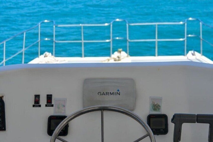 A boat's helm with a Garmin navigation device, a steering wheel, and a metal railing. 4