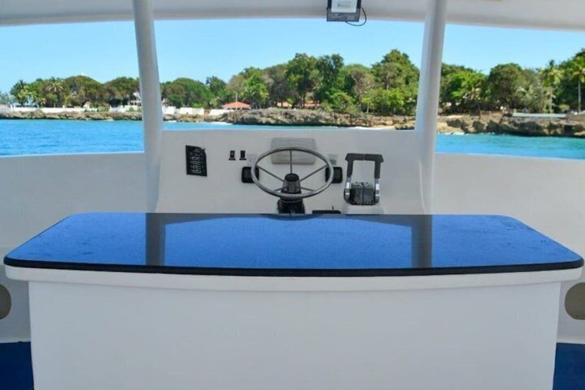 A boat's control station with a steering wheel, a small display, and a blue deck. 2