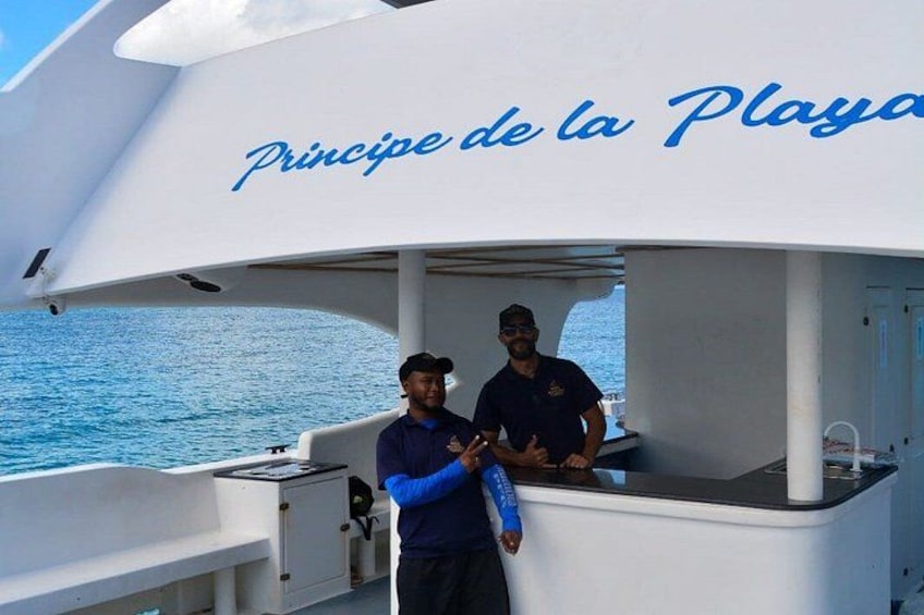 A boat with 'Principe de la Playa' written on the side, two people standing on the deck, and the ocean in the background. 5