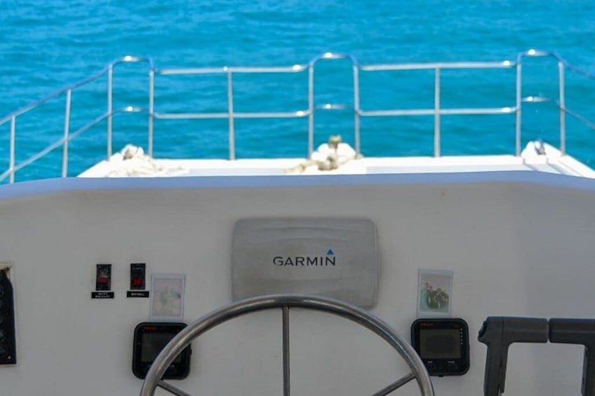 A boat's helm with a Garmin device, a steering wheel, and a metal railing. 4