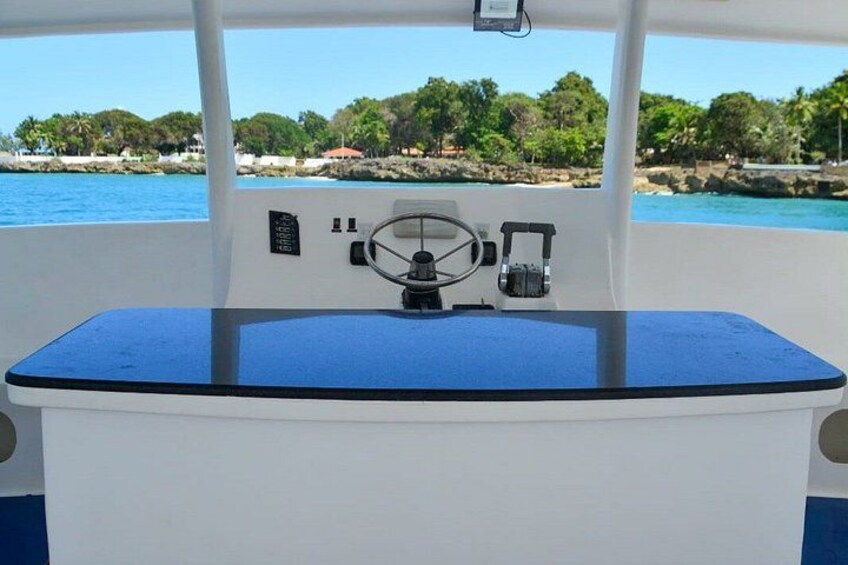 A boat's control station with a steering wheel, a control panel, and a blue deck. 2
