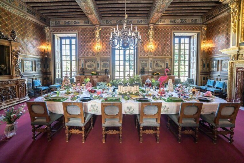 An ornate dining room with a large table set for a meal, surrounded by chairs and a chandelier. 4