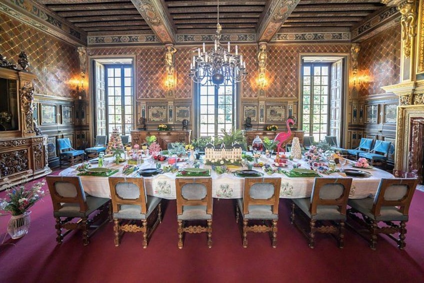 A grand dining room with ornate furniture, chandeliers, and a large table set for a meal. 4