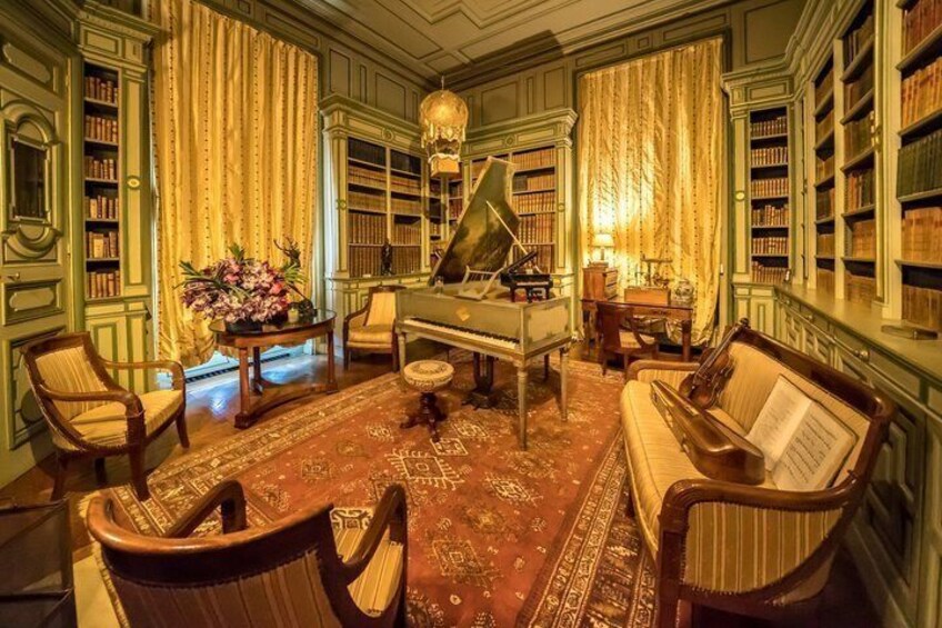 A library with a grand piano, bookshelves, a sofa, and a piano bench. 5