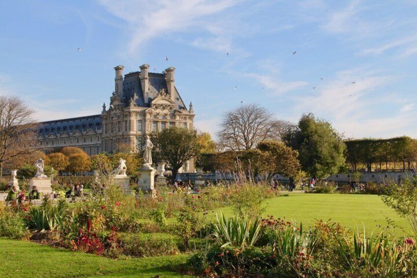 A large historic building with statues in a garden. 3