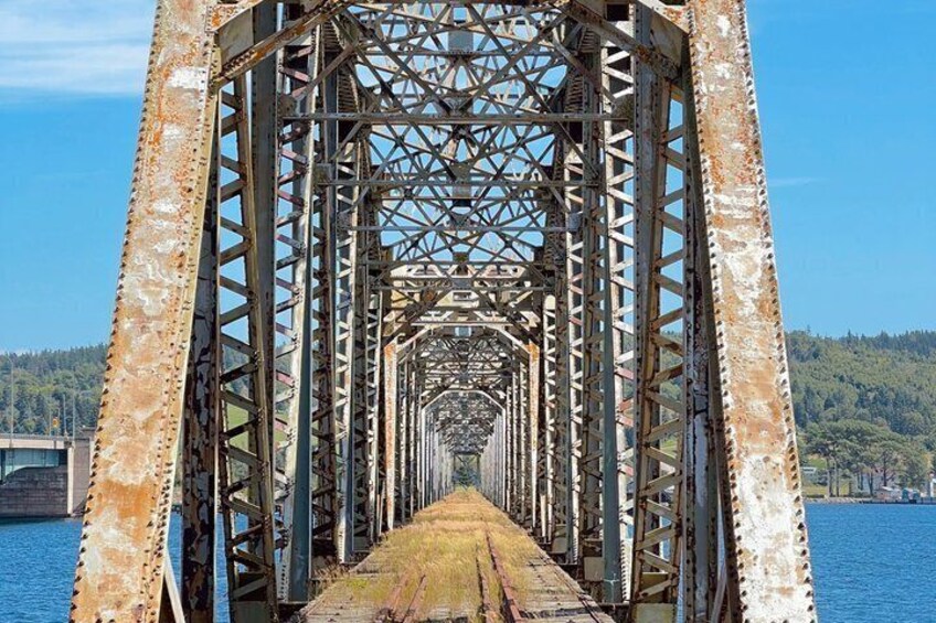 A rusted metal bridge with a clear view of the water and forested hills in the background. 3