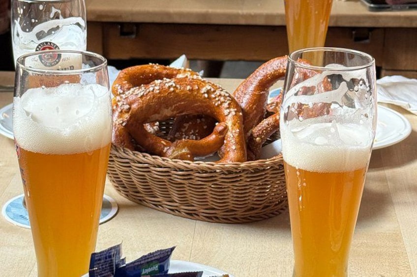 Two glasses of beer, a basket of pretzels, and a wooden table. 4