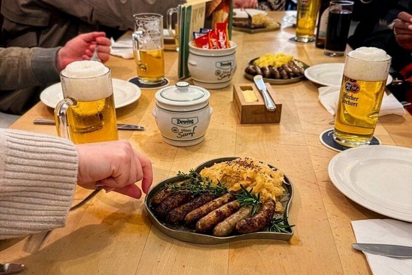 A dining table with food, beer mugs, and a hot plate of sausages. 4