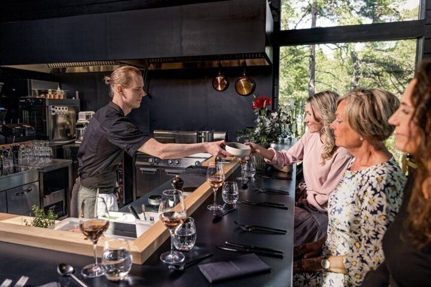 A chef serving wine to guests at a restaurant with a view of trees. 1