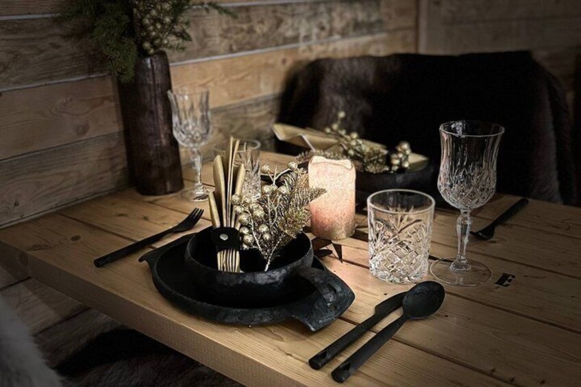 A wooden table with a candle, glassware, and a black bowl with utensils. 2