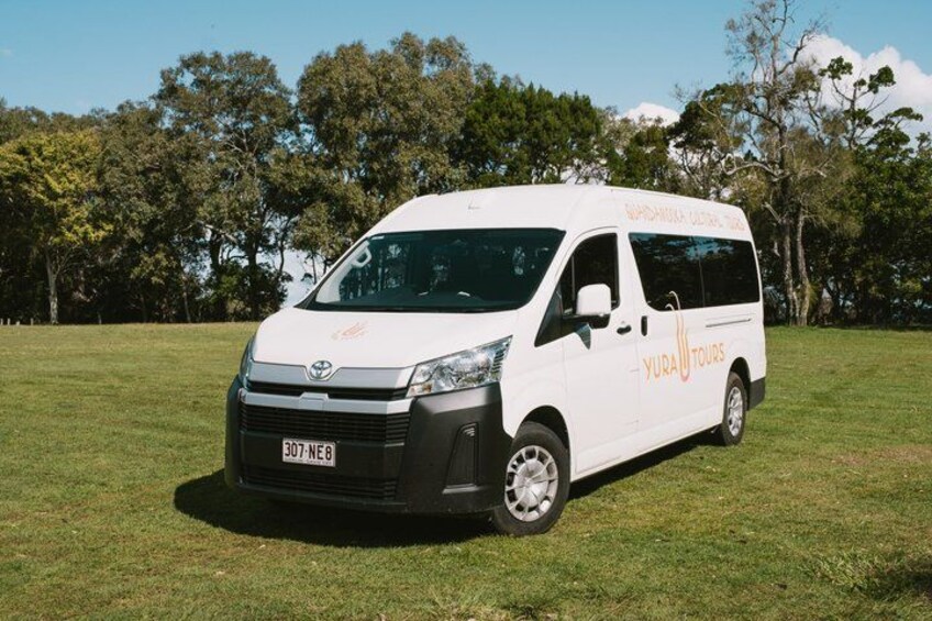 A white van with 'YURA TOURS' branding parked on grass with trees in the background. 5