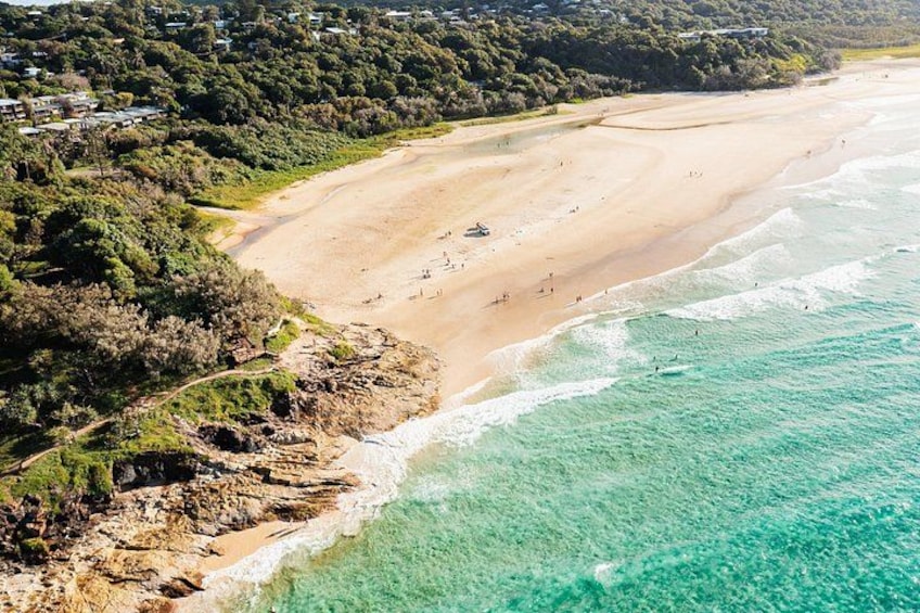 A coastal landscape with a sandy beach, clear turquoise waters, and a forested area. 4