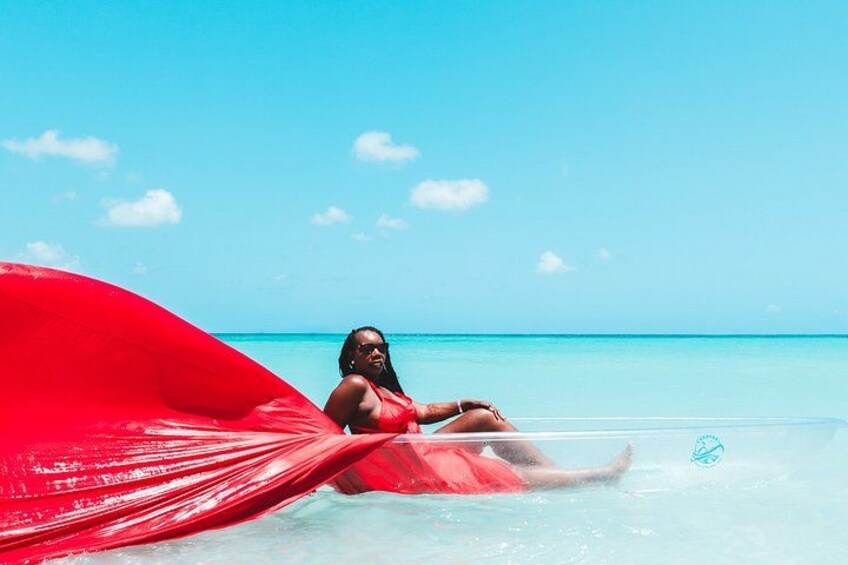 A person in a red swimsuit lying on a transparent inflatable float in clear turquoise water with a red fabric draped over them. 3