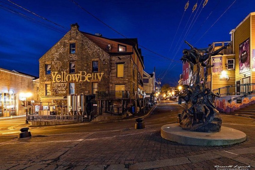 A historic building named YellowBerry Brewing House, a street with a central roundabout, and a statue in the foreground. 3