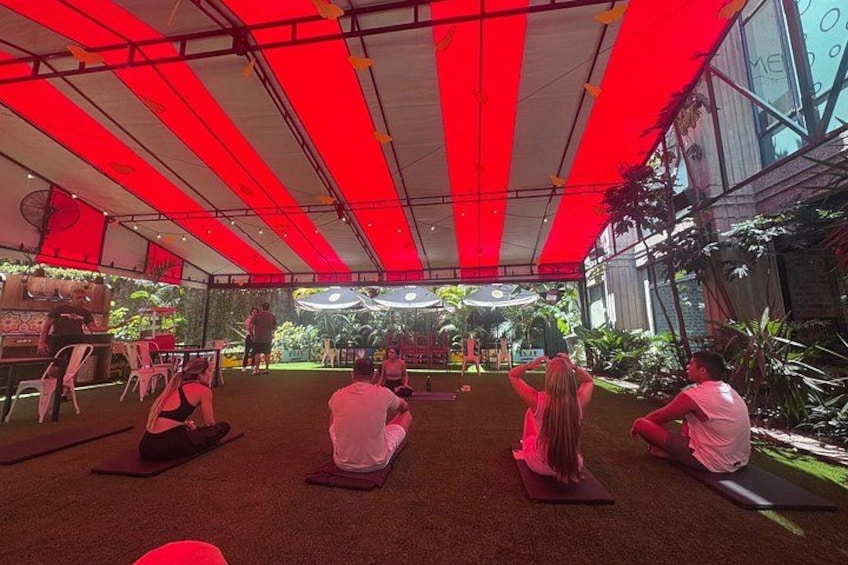 People sitting on yoga mats under a red canopy, with a stage and audience in the background. 4