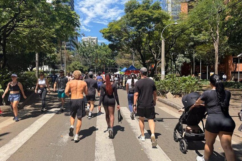 A group of people walking on a city street lined with trees and buildings. 3