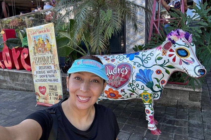 A person taking a selfie with a colorful, decorated horse statue in the background. 3