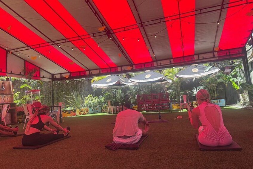 A yoga class in a tented area with red lighting, exercise mats, and a stage with speakers. 2