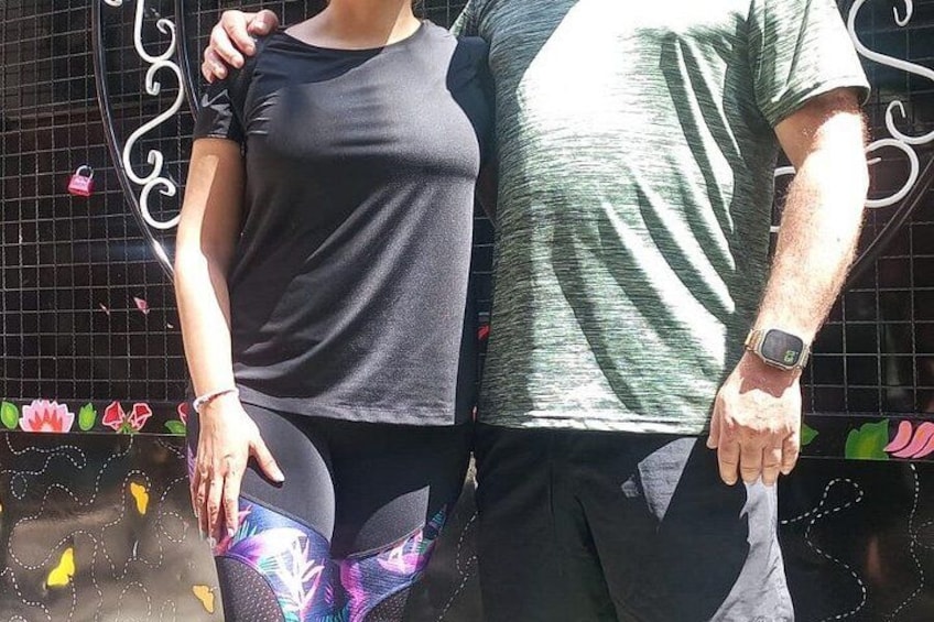 Two people standing close together, one wearing a black shirt and the other in a green shirt, with a decorative fence in the background. 5