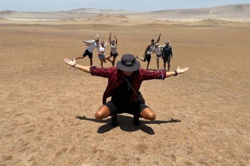 A person in a red plaid shirt and hat crouching in a desert with arms outstretched. 2
