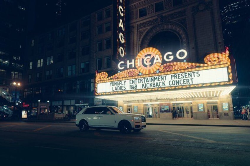 A white car parked in front of the Chicago Theatre with a marquee advertising a concert. 2