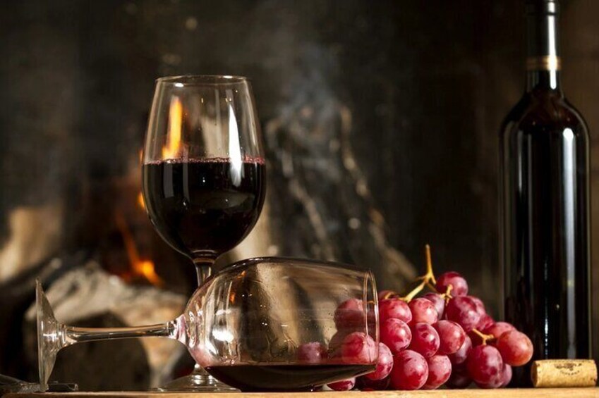 A glass of red wine, a bottle of wine, and a bunch of red grapes on a wooden surface. 5