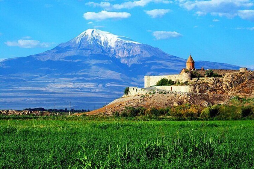 A snow-capped mountain, a historic building, and a green field. 3