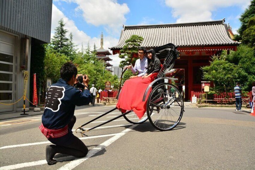 A person taking a photo of a traditional Japanese building with a red roof and a person in a wheelchair in the foreground. 4