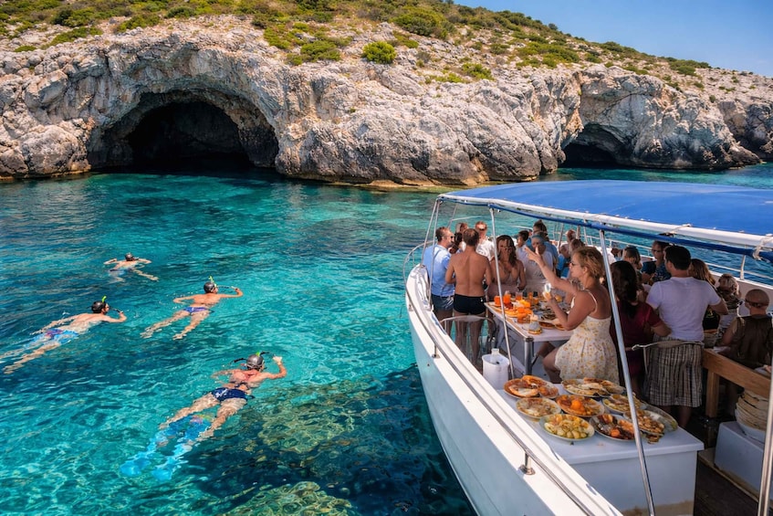 People swimming in clear blue water, a rocky cave, and a boat with passengers dining. 3