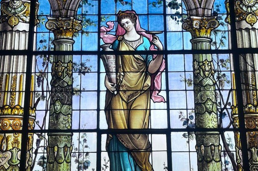 A stained glass window with a central figure, ornate columns, and floral patterns. 1