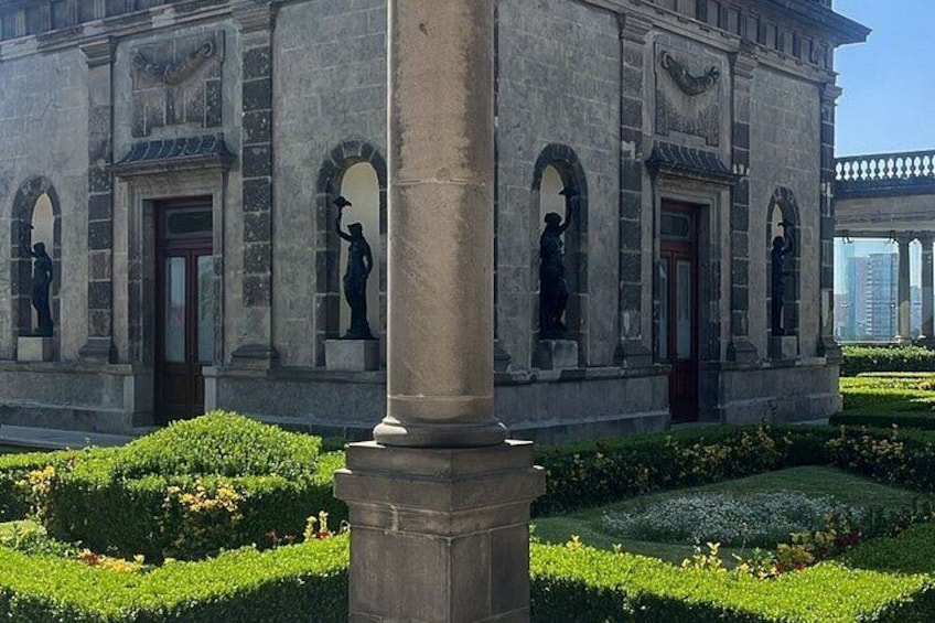 A stone building with statues, a well-maintained garden, and a clear sky. 5