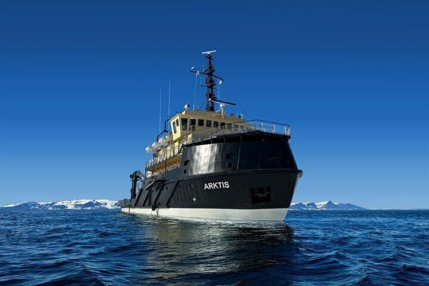 A large ship named ARKTIS sailing on blue waters with snow-capped mountains in the background. 1