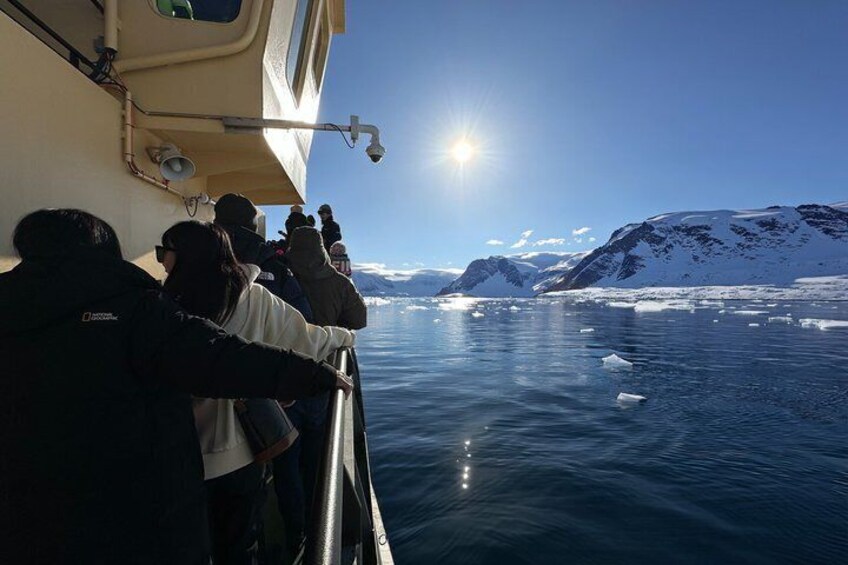 A group of people on a boat, observing icebergs and mountains in a clear, sunny day. 5