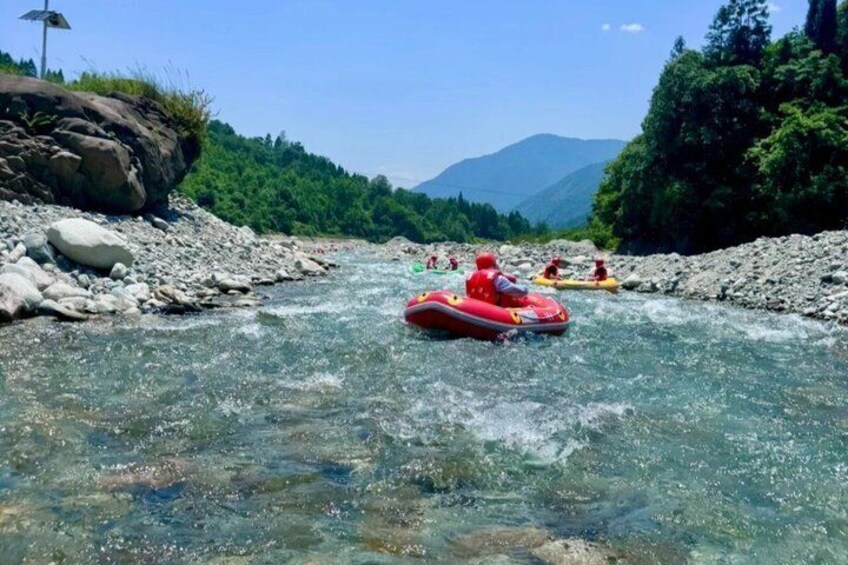A river with clear water, surrounded by rocks and greenery, with people rafting. 3