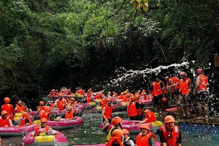 People in orange life vests on inflatable rafts in a water body surrounded by dense greenery. 1