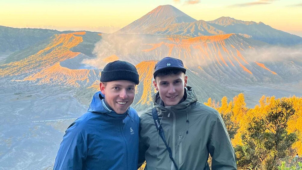 Two people standing in front of a mountain with a volcanic landscape in the background. 1