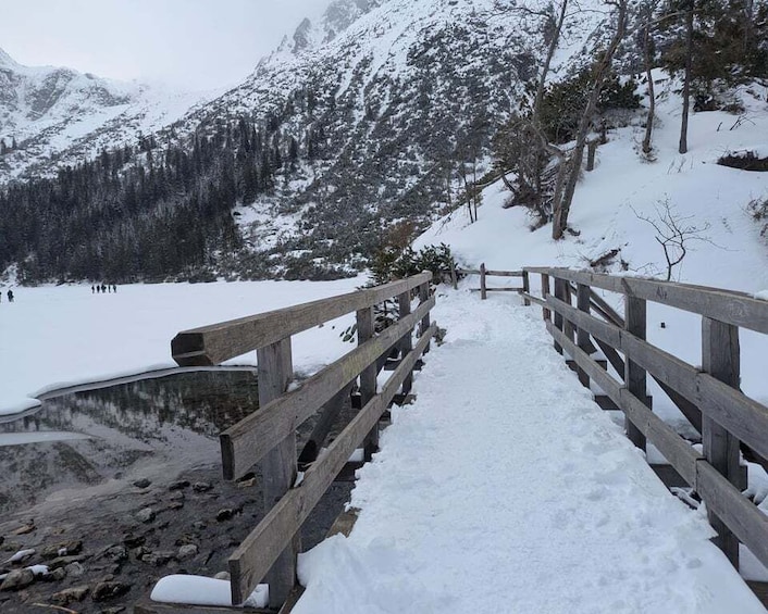 A wooden bridge over a snow-covered lake with mountains in the background. 1