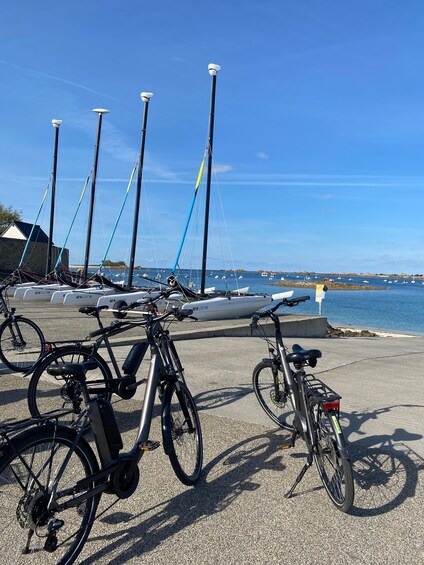 Bicycles parked near a waterfront with sailboats and a stone building in the background. 2