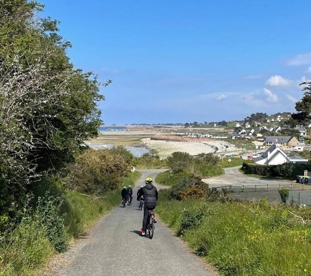 A paved path with cyclists, coastal landscape, and houses in the background. 5